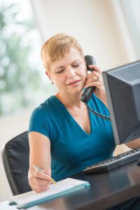 Businesswoman Using Landline Phone While Working At Desk