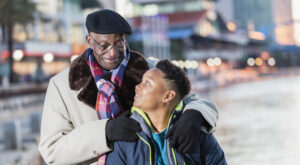An African-American boy, 10 years old, standing in the city with his great grandfather, a senior man in his 70s. They are looking at each other affectionately, smiling.