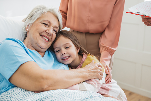 Woman with daughter visiting her mother at hospital, she is talking with doctor and showing love and care for her mother.