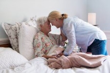 Hospice patient in bed touching foreheads with caregiver