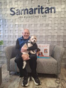 Hospice volunteer holding a puppy with a robotic companion pet next to him