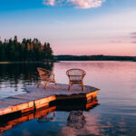 Two wooden chairs on a wood pier overlooking a lake at sunset