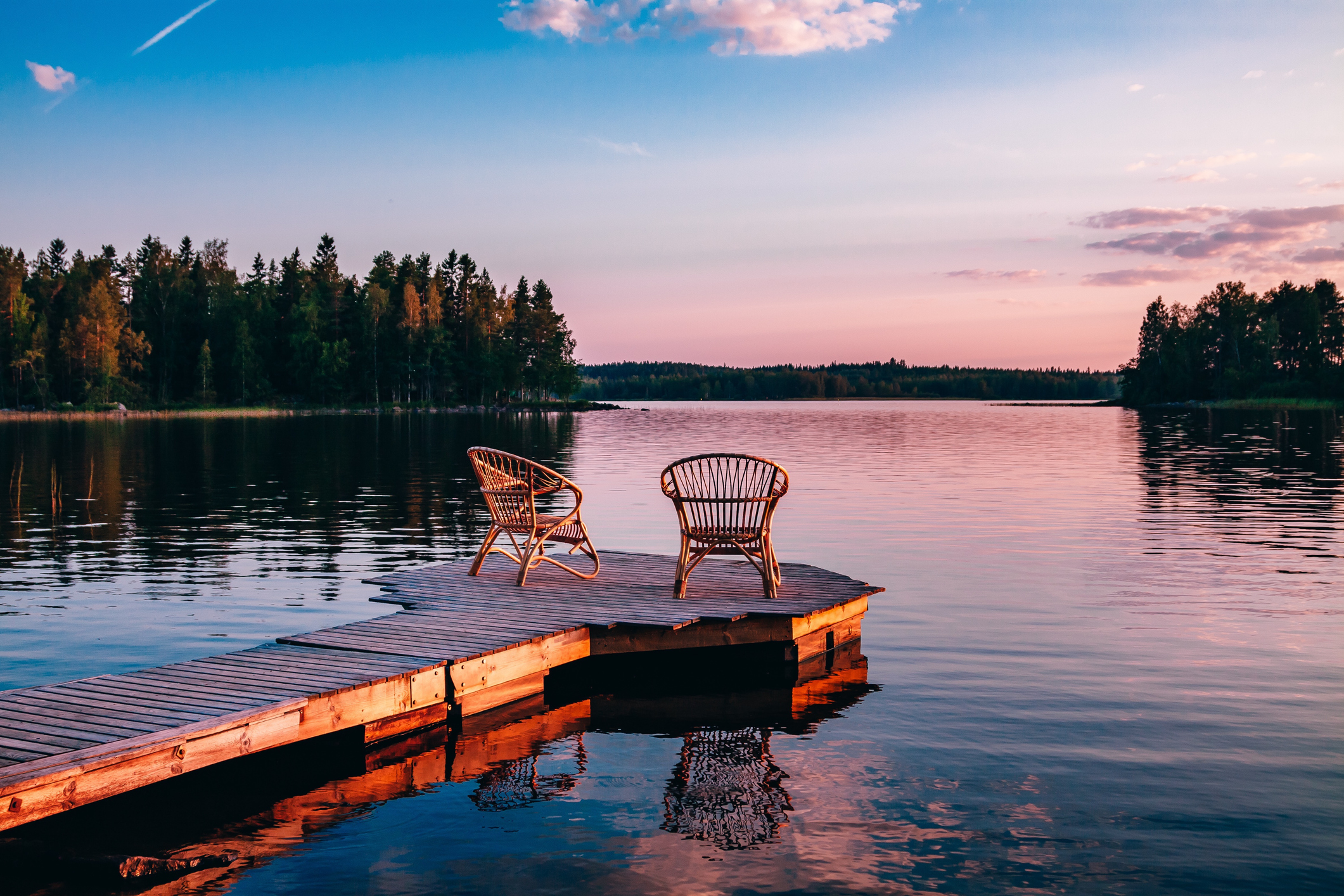 Two wooden chairs on a wood pier overlooking a lake at sunset