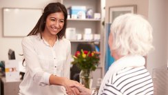 Receptionist Greeting Female Patient At Hearing Clinic, Smiling Shaking Hands