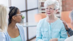 Caucasian senior woman cries while talking about hard issues during a senior adult support group. An unrecognizable man comforts her while she speaks.
