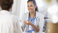 Confident mid adult African American doctor gestures while talking with an unrecognizable female patient. The doctor is reviewing the patient's prescription medication.