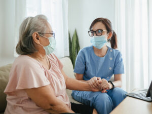 A home health aide and patient at a desk wearing masks