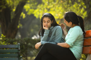 Young woman sitting looking sad with head in palm. Older woman sitting next to her comforting her. 