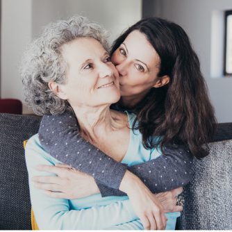 woman kissing senior mother and hugging her from back