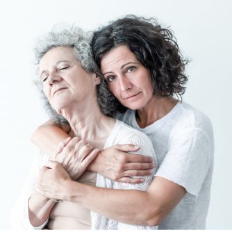 serious adult daughter embracing senior mother